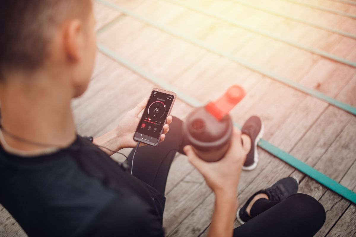 športnik drži steklenico vode in telefon